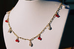 Load image into Gallery viewer, White mannequins chest wearing the Anastasia necklace, shining in the sunlight. The necklace is a gold filled satelite chain with five pearls and four red swarovski crystals interchanging.
