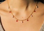 Load image into Gallery viewer, Lady wearing a grey top wearing the Anastasia necklace, the frame is focused on the chest area to bring focus to the necklace and is taken in sunlight. The necklace is a gold filled satelite chain with five pearls and four red swarovski crystals interchanging.
