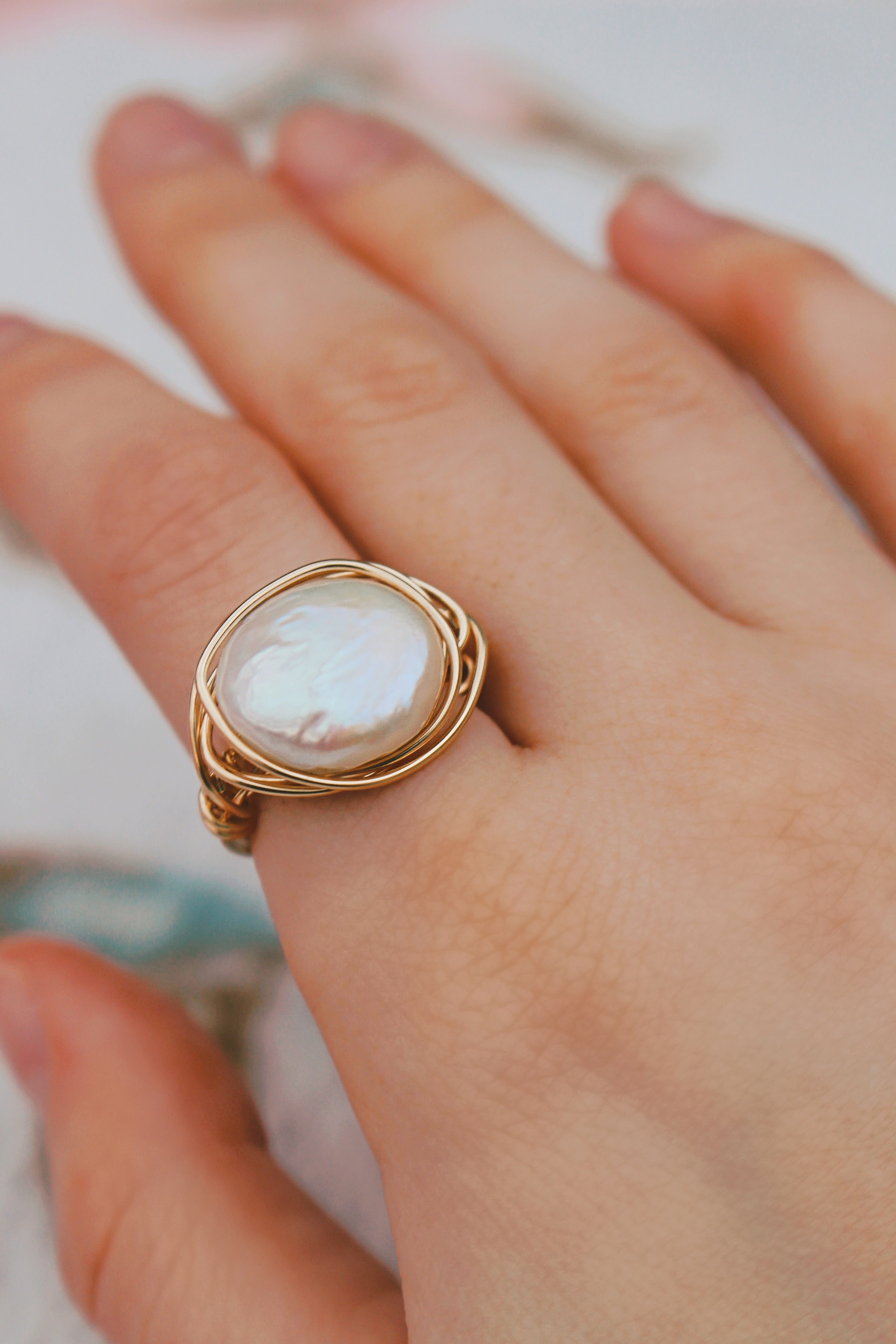 Photo is zoomed into a hand wearing a gold filled wire wrapped coin shaped freshwater pearl, handmade, ring on the pointer finger.