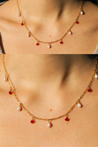Lady wearing a grey top wearing the Anastasia necklace, the frame is focused on the chest area to bring focus to the necklace and is taken in sunlight. The necklace is a gold filled satelite chain with five pearls and four red swarovski crystals interchanging.